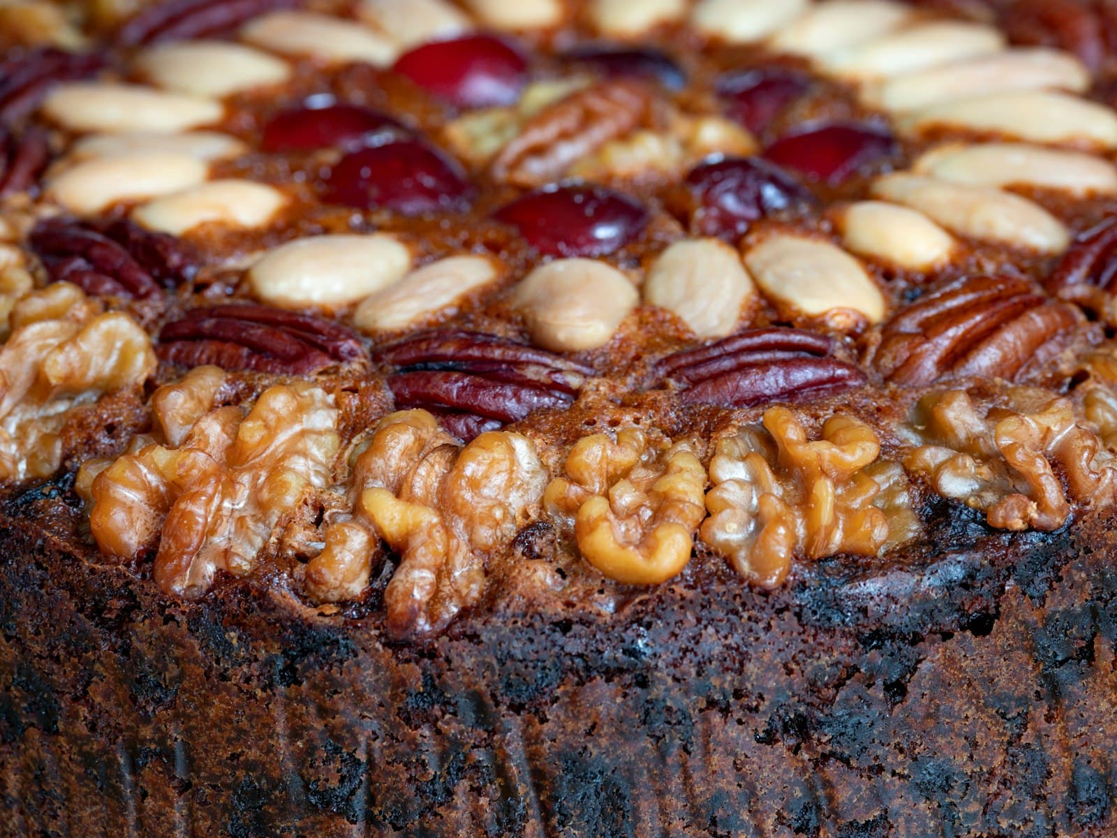 Close-up of a rich fruit cake studded with almonds, walnuts and glacé cherries.
