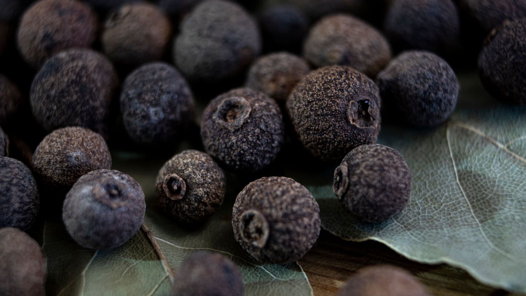 Whole allspice berries resting on dried bay leaves.