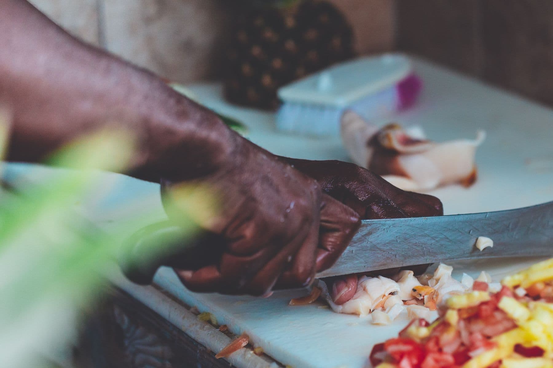 Hands chopping fresh ingredients on a board in a Caribbean kitchen.