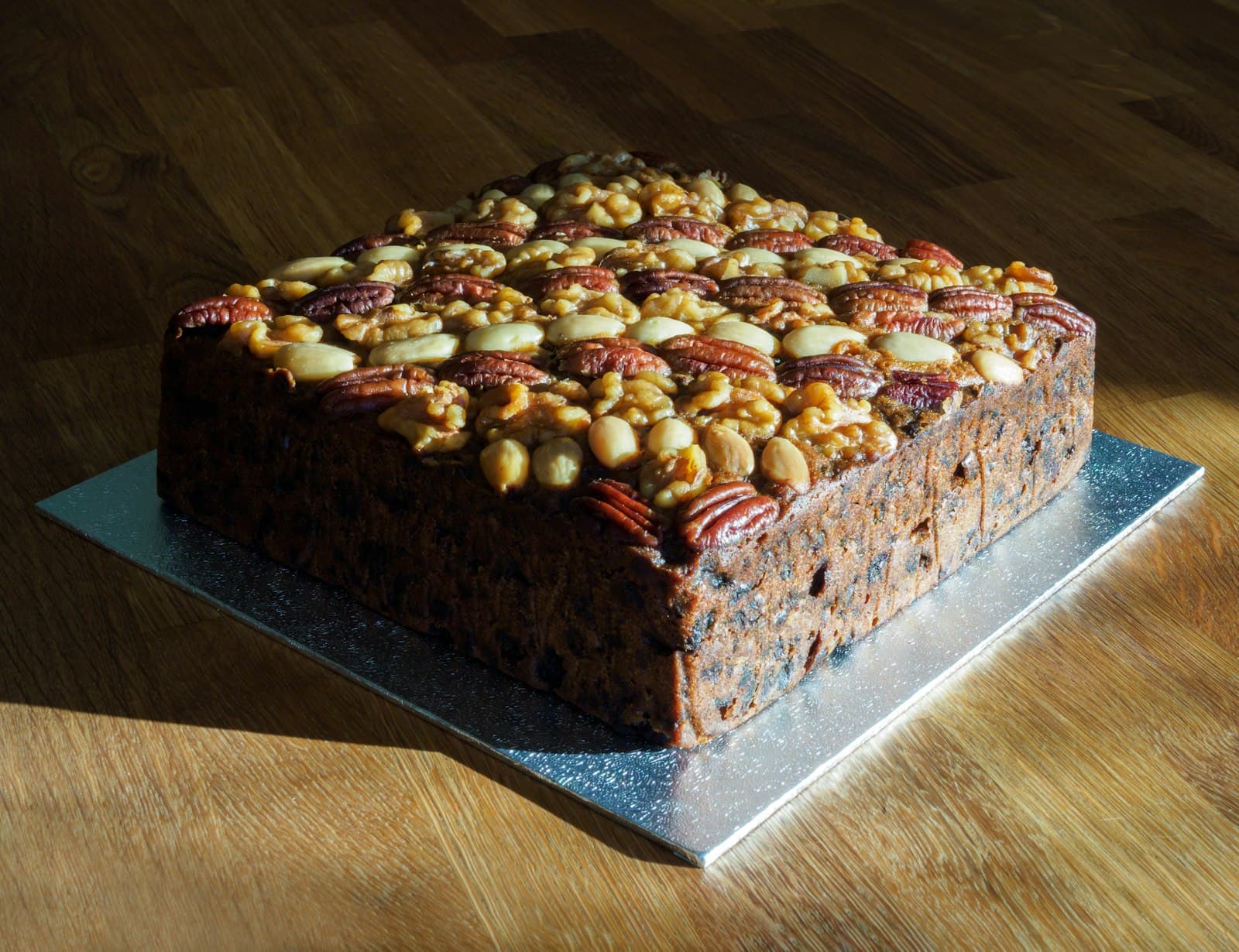 A whole Caribbean fruit cake topped with glazed nuts on a silver board.
