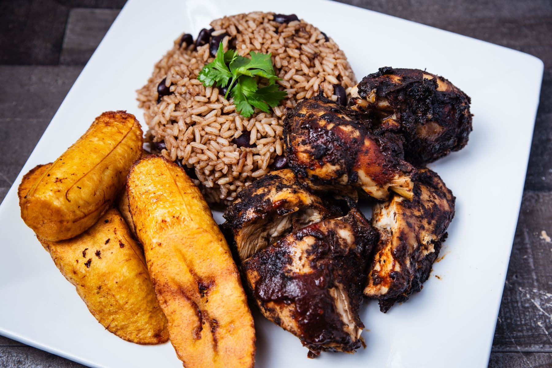 Jerk chicken with rice and peas and fried plantain on a plate.