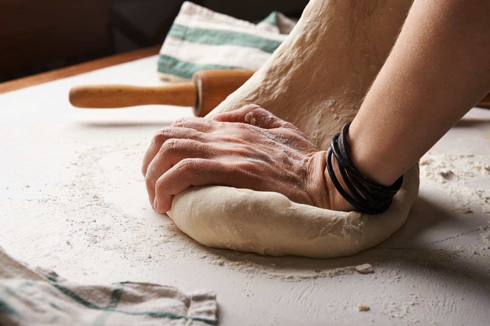 Hands working dough on a floured surface.